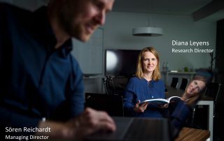 Sören Reichardt, Managing Director, blurred in the foreground on his laptop, Focus on Diana Leyens, Research Director, with book in the background